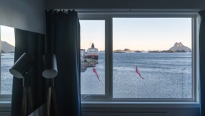 Una habitación con un amplio ventanal que ofrece vistas al mar, un barco y montañas distantes.