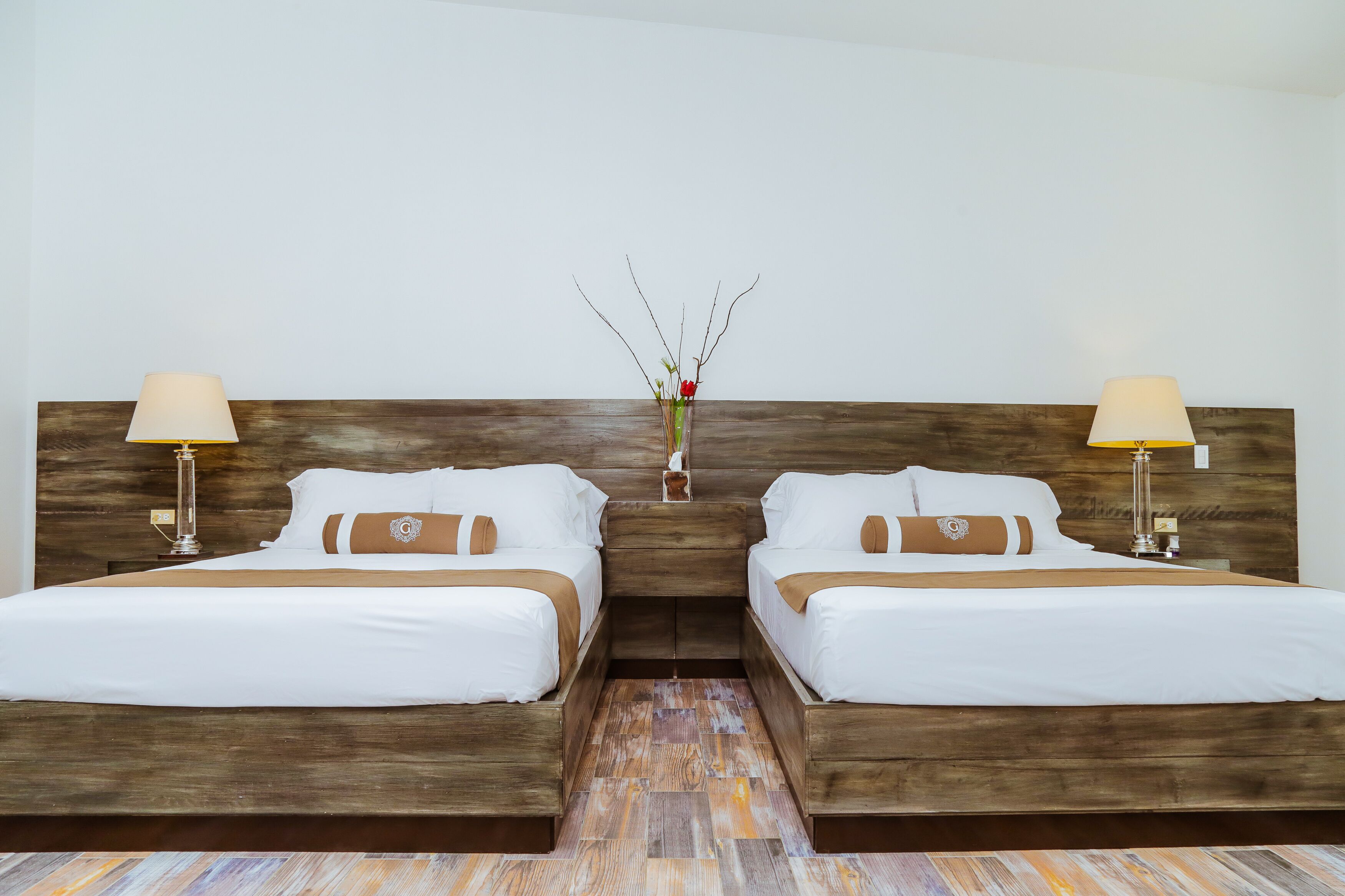 Una habitación de hotel con dos camas individuales, cabeceros de madera, ropa de cama blanca y lámparas de noche.