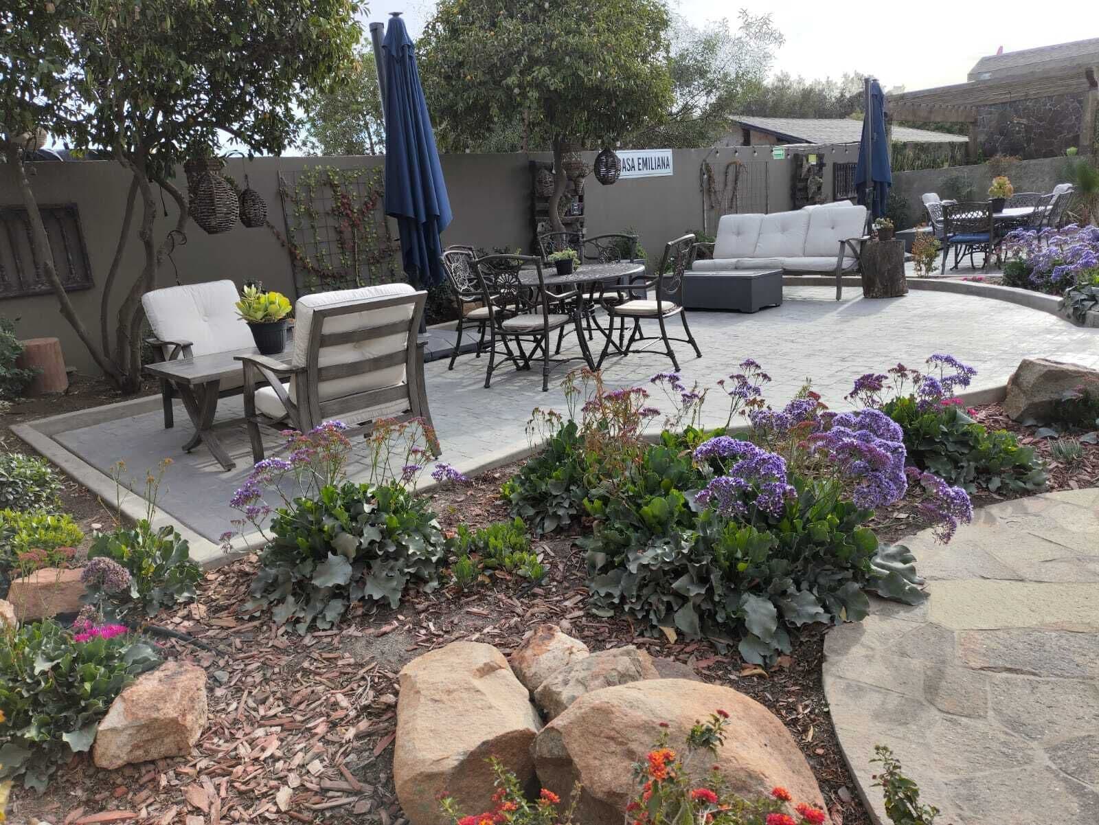 An outdoor patio area with a seating arrangement, a stone pathway, and a variety of plants and flowers.