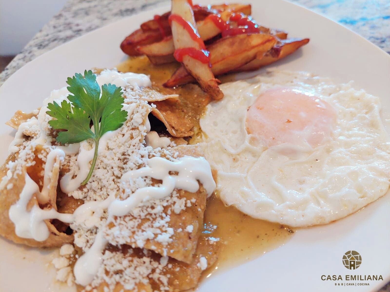 Un plato de comida con enchiladas, un huevo frito y patatas a la francesa.
