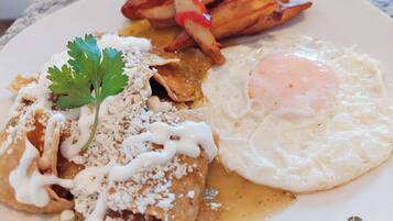 Un plato de comida con enchiladas, un huevo frito y patatas a la francesa.