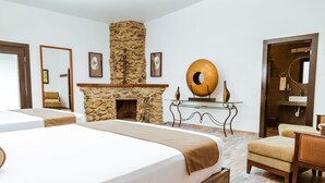 A hotel room with two beds, a stone fireplace, a round mirror, and a wooden door. - Casa Emiliana (Valle de Guadalupe)