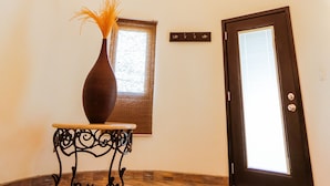 A hallway with a wooden ceiling, a chandelier, a vase on a table, and a door with a window. - Casa Emiliana (Valle de Guadalupe)