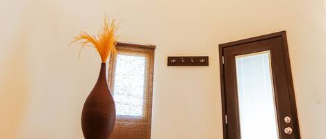 A hallway with a wooden ceiling, a chandelier, a vase on a table, and a door with a window.