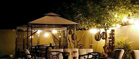 Un patio exterior con un área de estar techada, mesas y sillas.