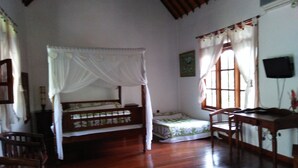 A room with a wooden floor, a bed with a canopy, a desk, chairs, and a television on the wall. - Puri Eling Blimbingsari (Melaya)