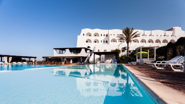 A swimming pool with lounge chairs and a building with multiple balconies in the background. - Mursia Resort & Spa (Pantelleria)