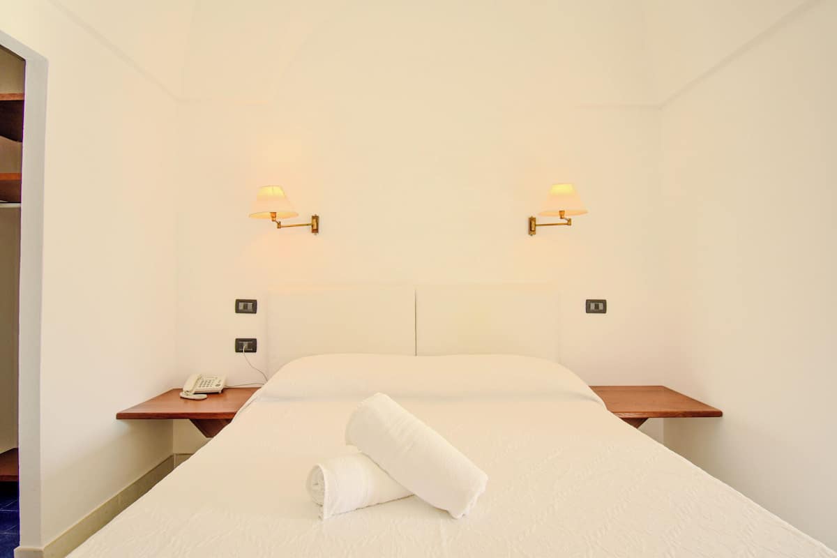 Hotellihuone, jossa on suuri sänky, kaksi yöpöytää, puhelin ja seinään kiinnitetyt lamput.