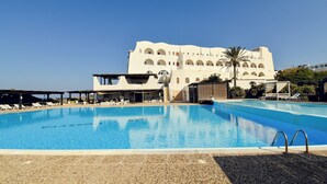 A swimming pool with lounge chairs and a covered area, a building with arched windows, and a clear blue sky. - Mursia Resort & Spa (Pantelleria)