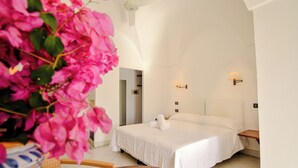 A hotel room with a large bed, a bedside table, a wall-mounted lamp, and a potted plant. - Mursia Resort & Spa (Pantelleria)