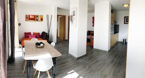 A modern living space with a dining area, kitchen, and a cozy seating area with a sofa and cushions.