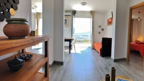 A hotel corridor with a wooden table, a bowl, and a vase on the left. A bed with a red blanket is visible in the background. - Magnificent T2 on the ground floor with pool in Alata in southern Corsica (Alata)