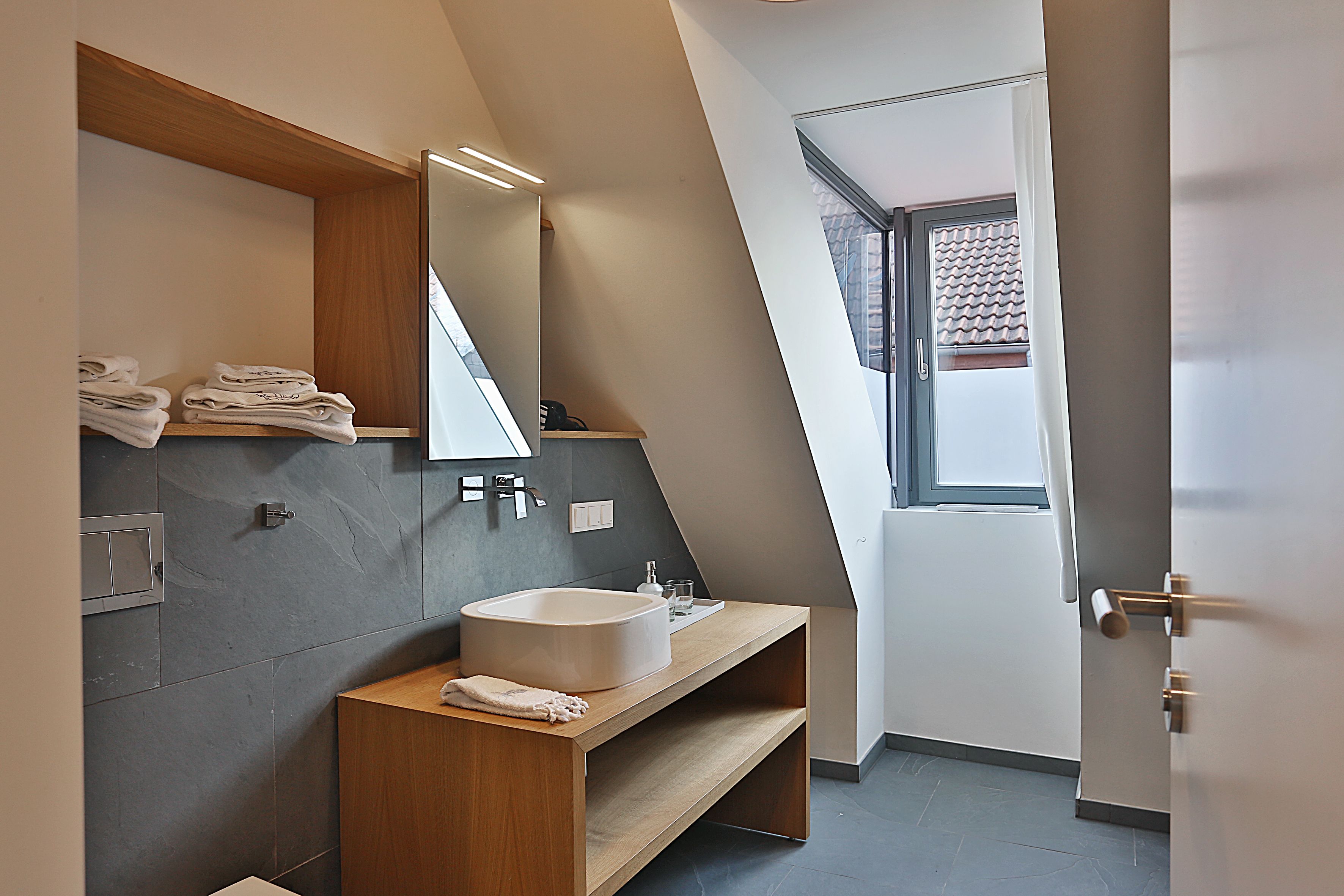 A modern bathroom with a built-in sink, a wooden vanity, a large mirror, and a towel rack.