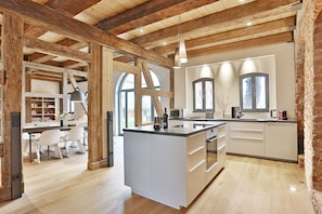 Una cocina moderna con una isla grande, vigas de madera y una zona de comedor con sillas blancas.