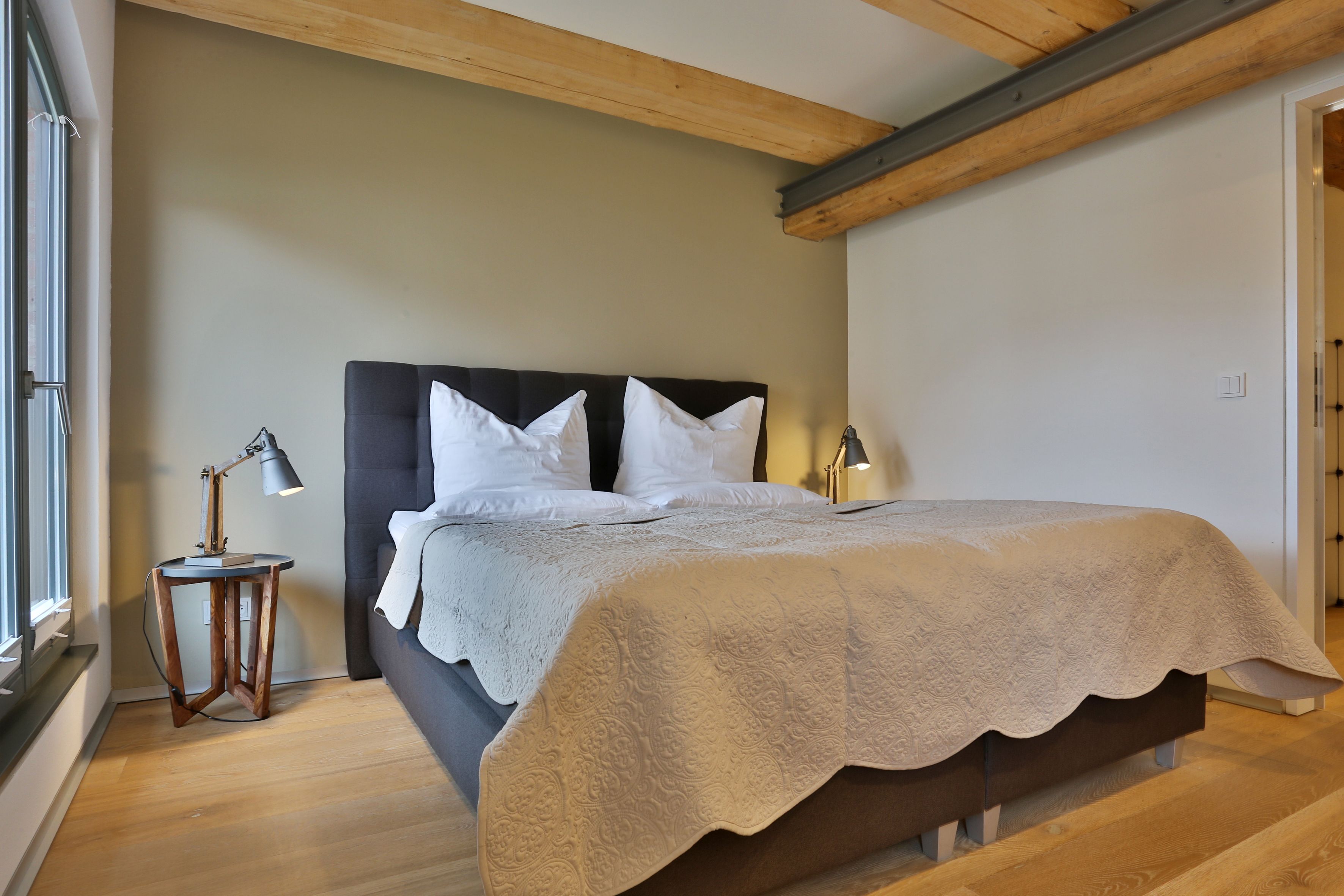 Een slaapkamer met een bed, een nachtkastje met lamp en een raam.