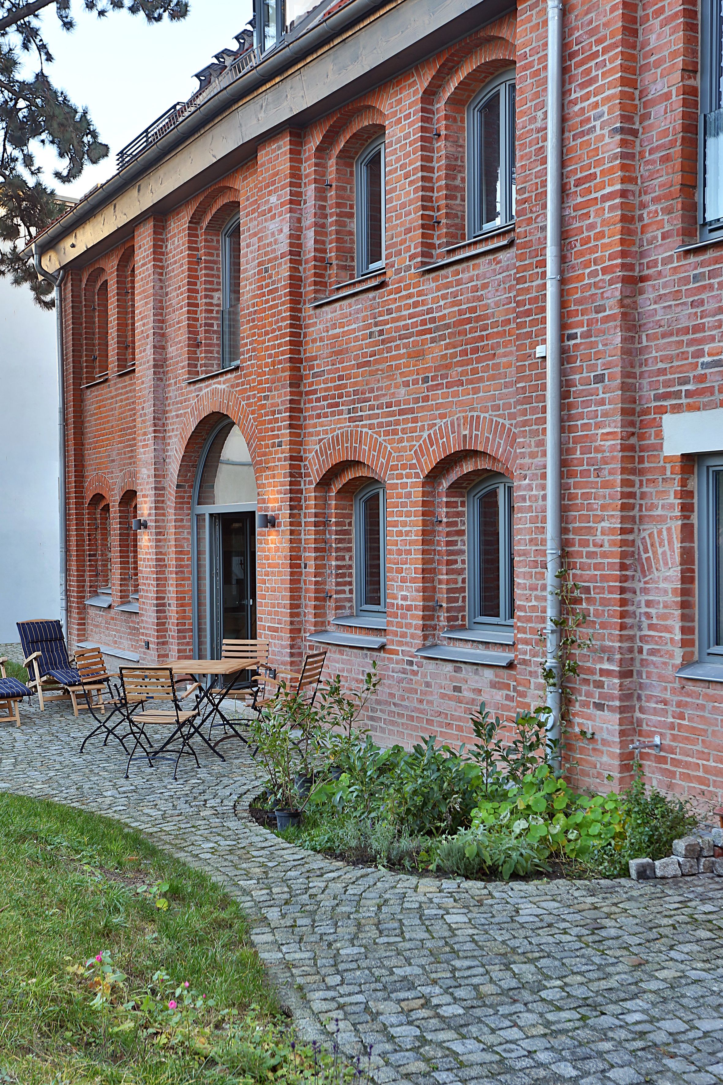 A red brick building with arched windows and a paved patio area with outdoor furniture.