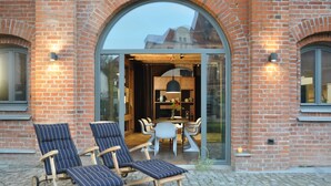 A brick building with a large arched entrance, a glass door, and a seating area with two lounge chairs and a table. - Backsteinspeicher Stralsund (Stralsund)
