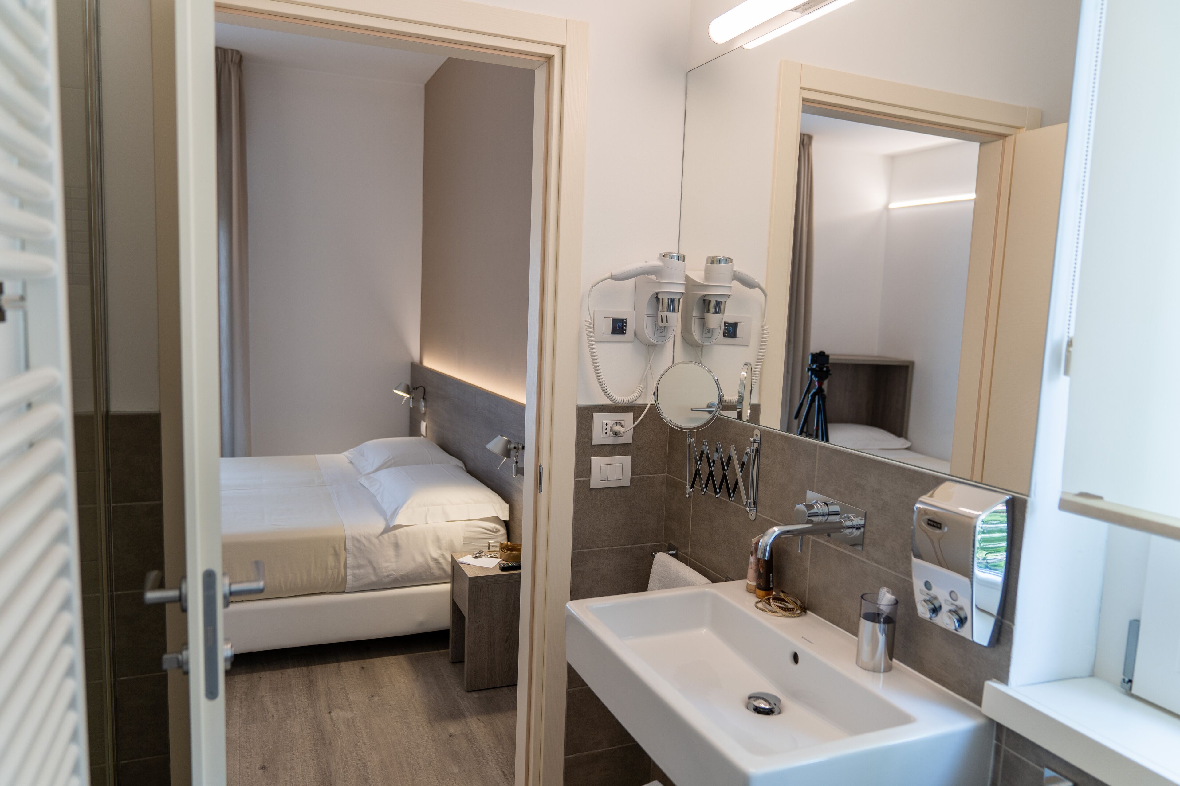 A modern hotel bathroom with a large sink, a mirror, and hair dryers mounted on the wall.