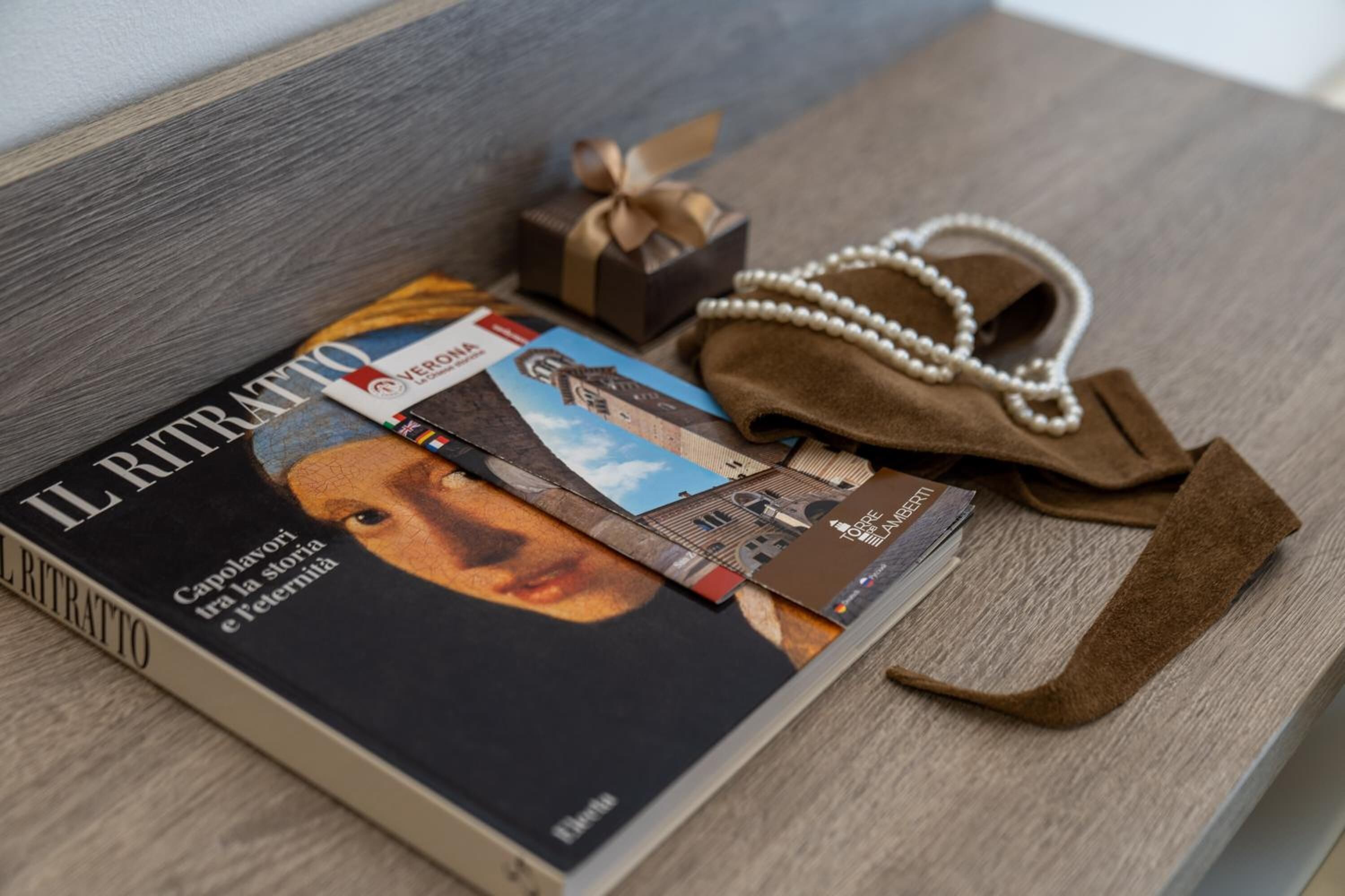 A magazine titled "IL RITRATTO" on a wooden surface with a brown leather bag and a pearl necklace.