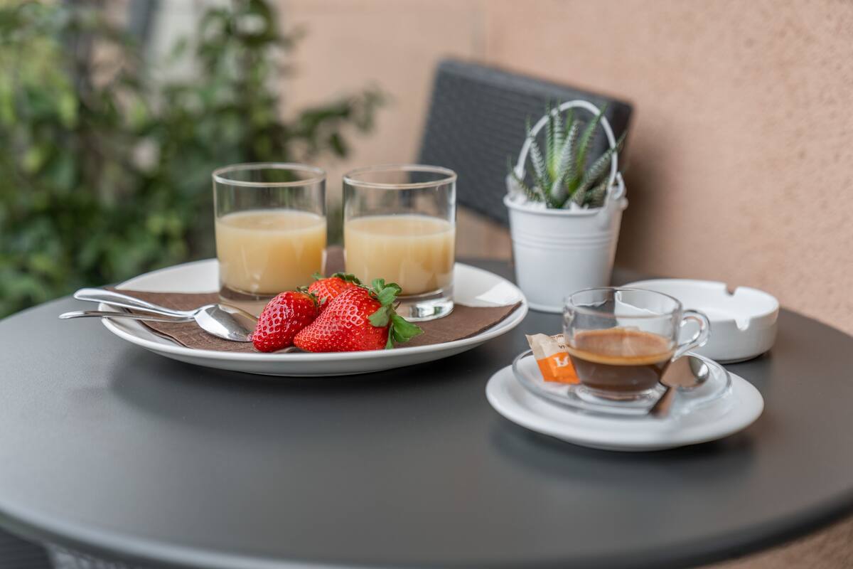 A table with a plate of strawberries and two glasses of juice, a cup of coffee, and a small potted plant.