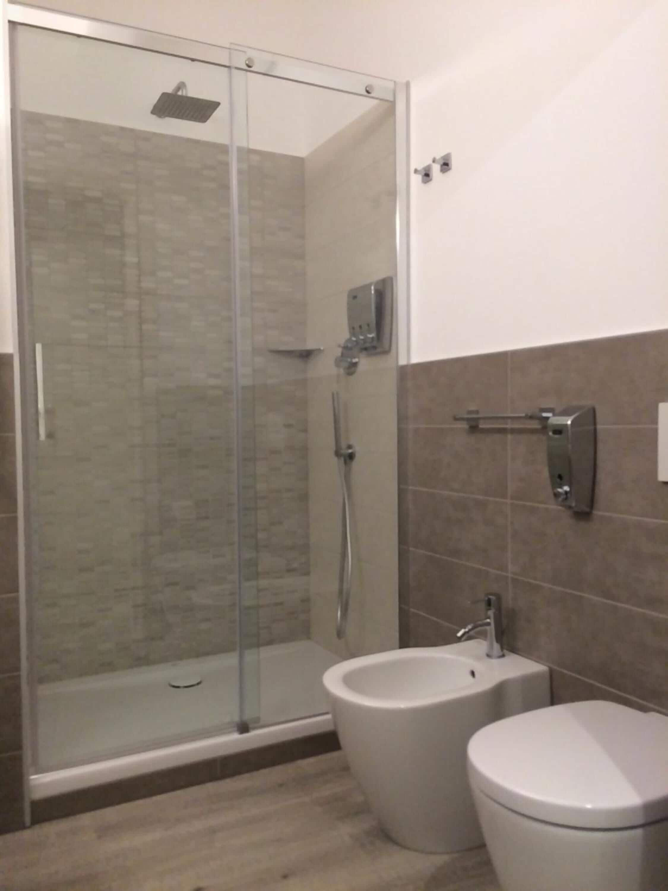 Une salle de bain moderne dotée d’une douche à parois de verre, de toilettes séparées et d’un bidet.
