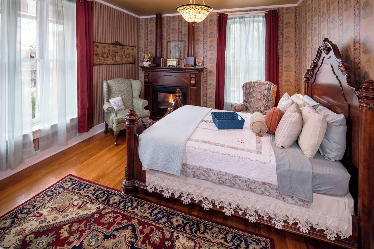 A traditional bedroom with a large bed, a fireplace, and a patterned rug.