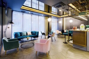 Un moderno vestíbulo de hotel con un sofá, sillas, una mesa de centro y una zona de bar.