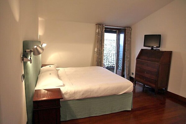 A bedroom with a bed, a dresser, a desk lamp, and a television.