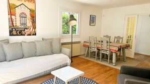 A living room with a sofa, a dining table with chairs, a small white table, and a patterned rug.