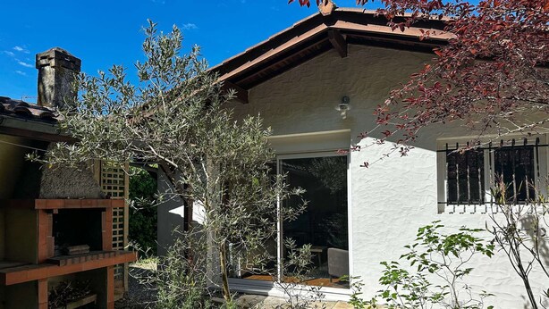 A house with a stone chimney, a wooden deck, and a garden with various plants.