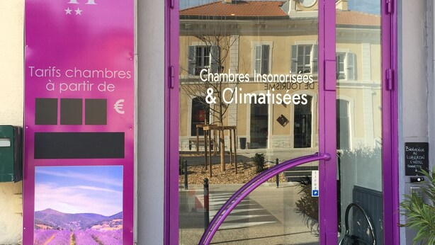 A hotel entrance with a purple door and a sign indicating it offers unisex and climate-controlled rooms. - Luberon L'hôtel (Apt)
