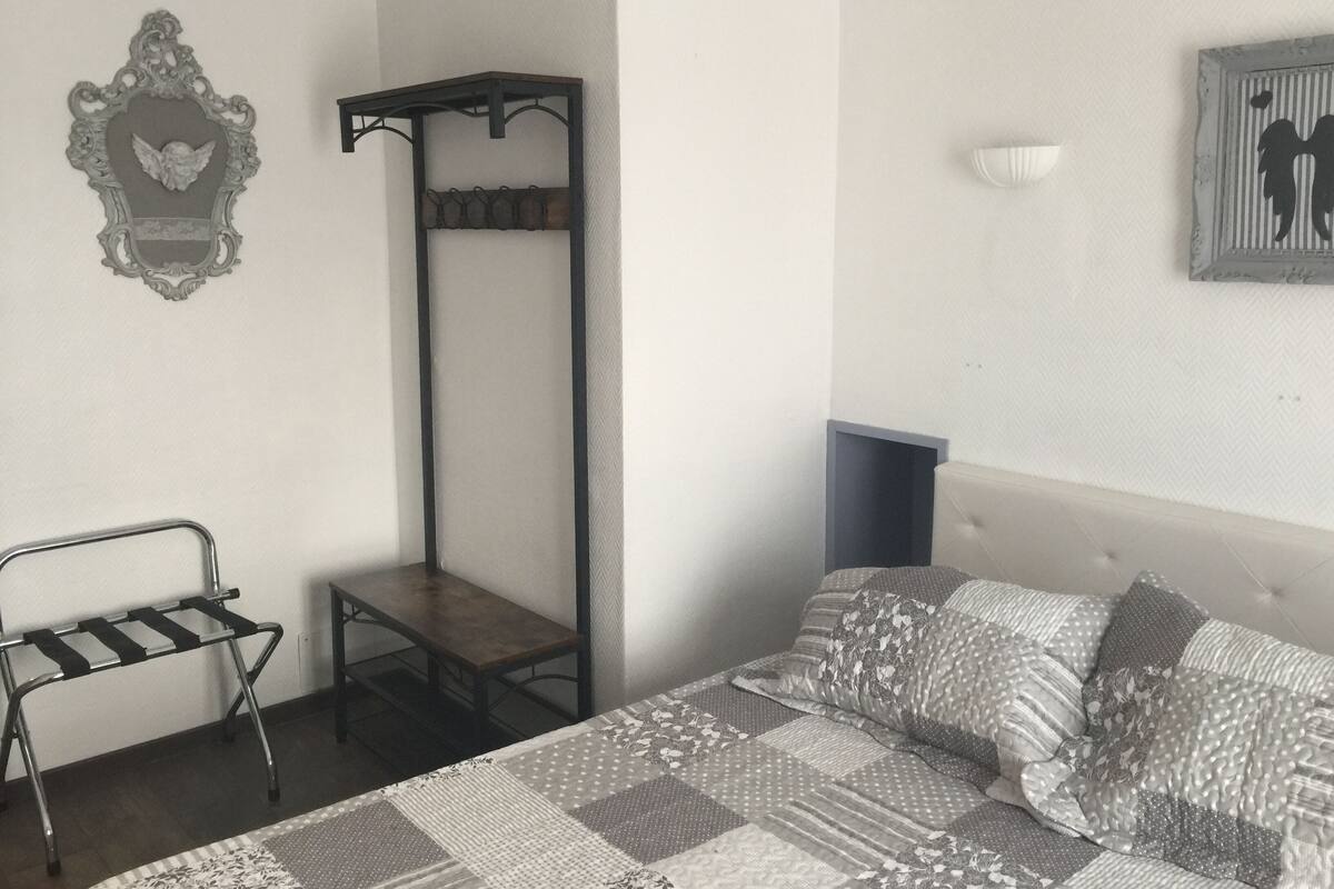 Quarto com cama, um banco de metal, prateleira na parede e quadro emoldurado.