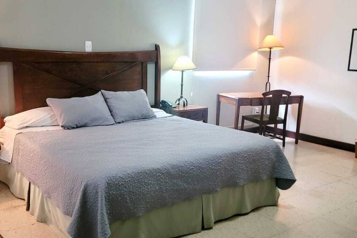 A neatly made bed with a wooden headboard, two bedside tables with lamps, a chair, and a framed picture on the wall.