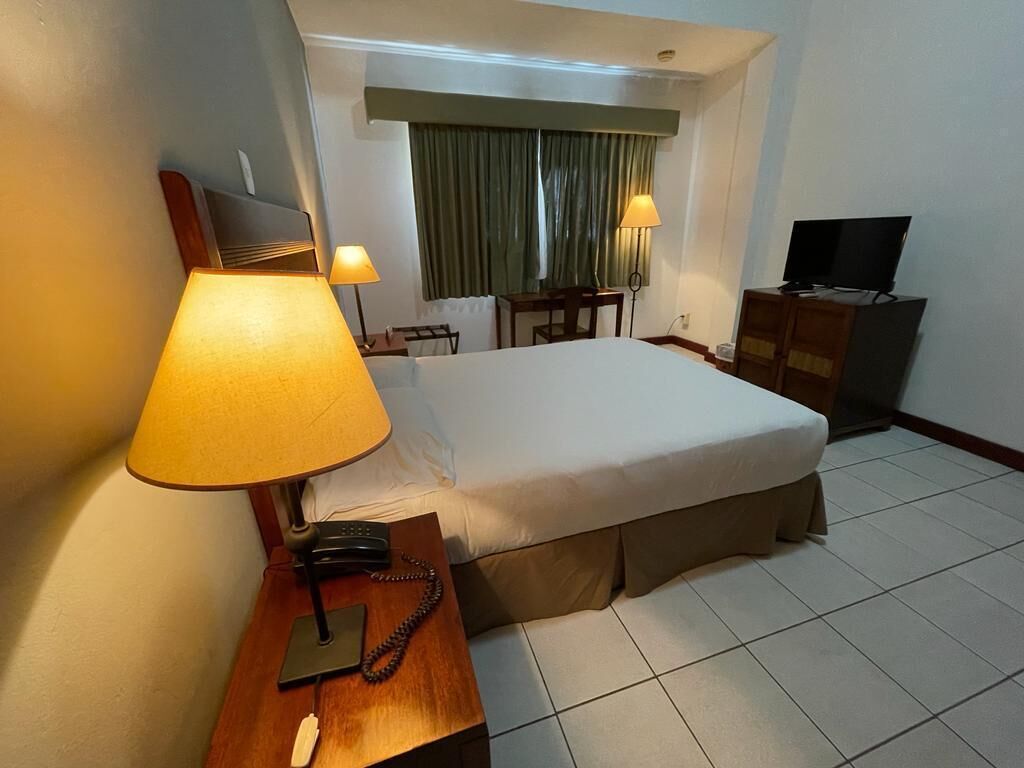 A hotel room with a bed, bedside lamps, a desk with a telephone, a television, and a small table with a chair.