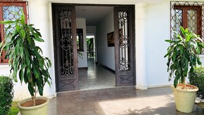 A building entrance with a tiled floor, two large potted plants, and decorative iron gates. - Hotel Casa del Sol (Managua)