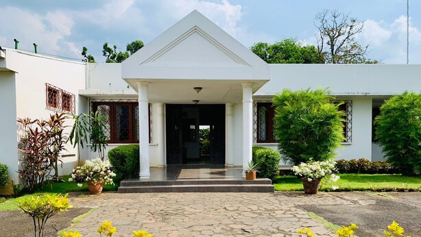 A white building with a central entrance, stone pathway, and surrounding greenery. - Hotel Casa del Sol (Managua)