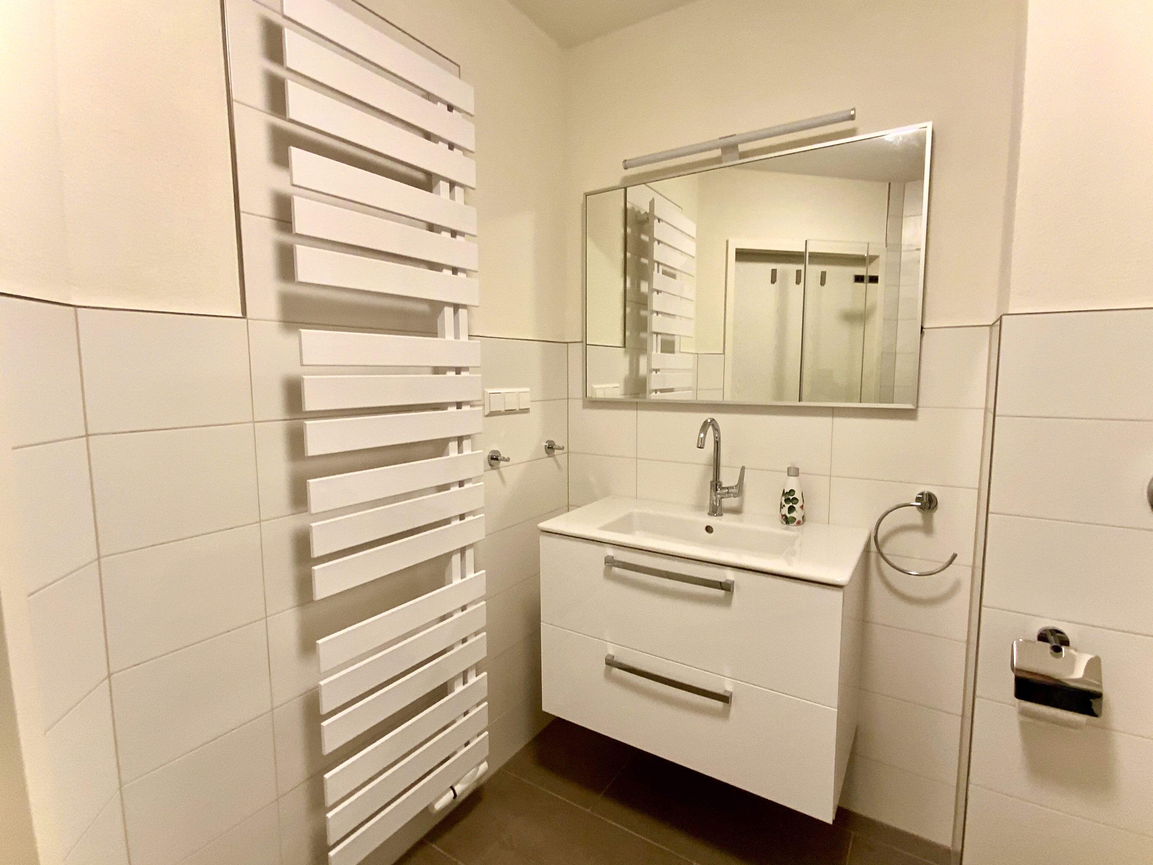 A modern bathroom with a white vanity, a mirror, and a towel rack.