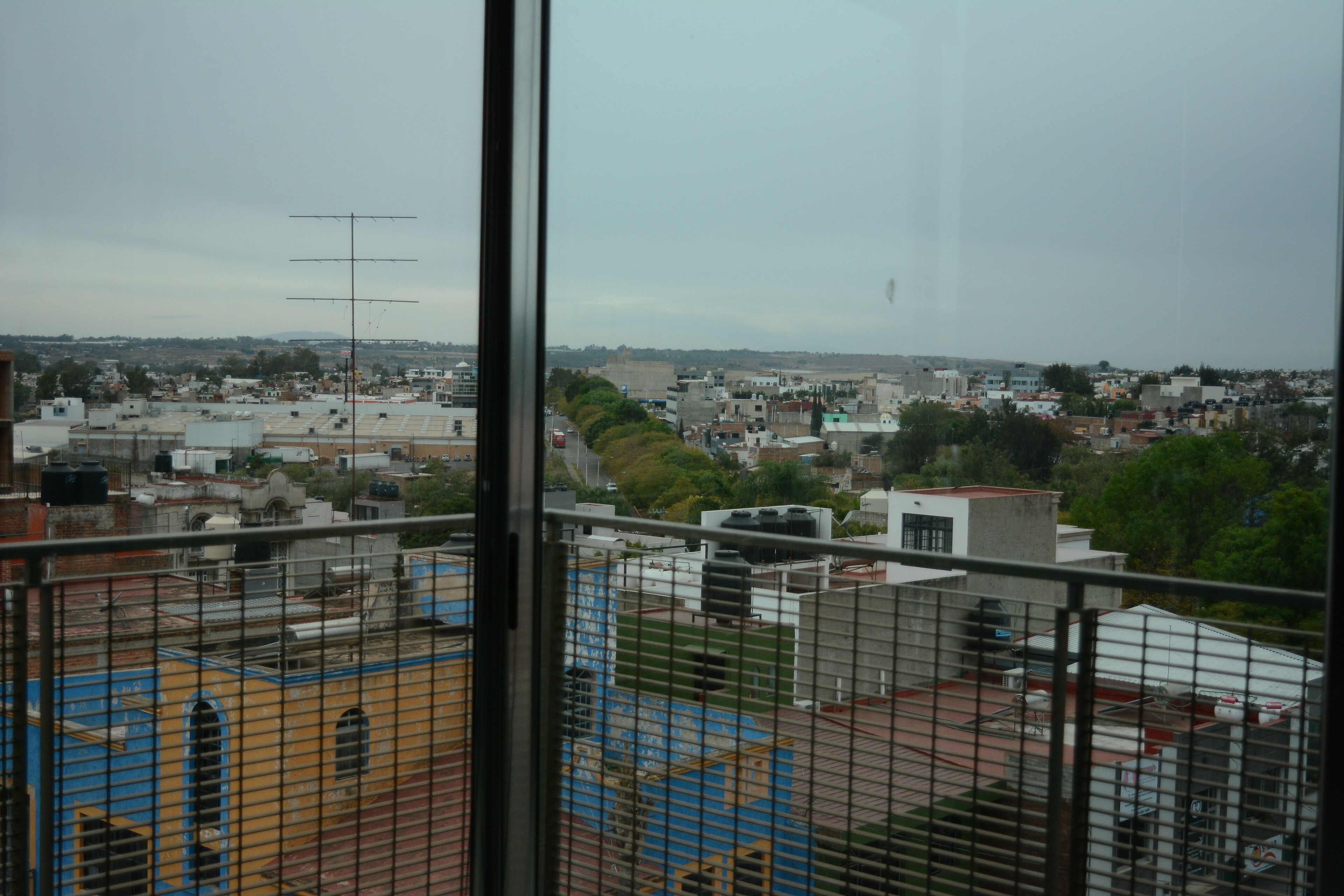 Une vue depuis une fenêtre donnant sur un paysage urbain, avec des immeubles, un terrain de sport et une colline au loin.
