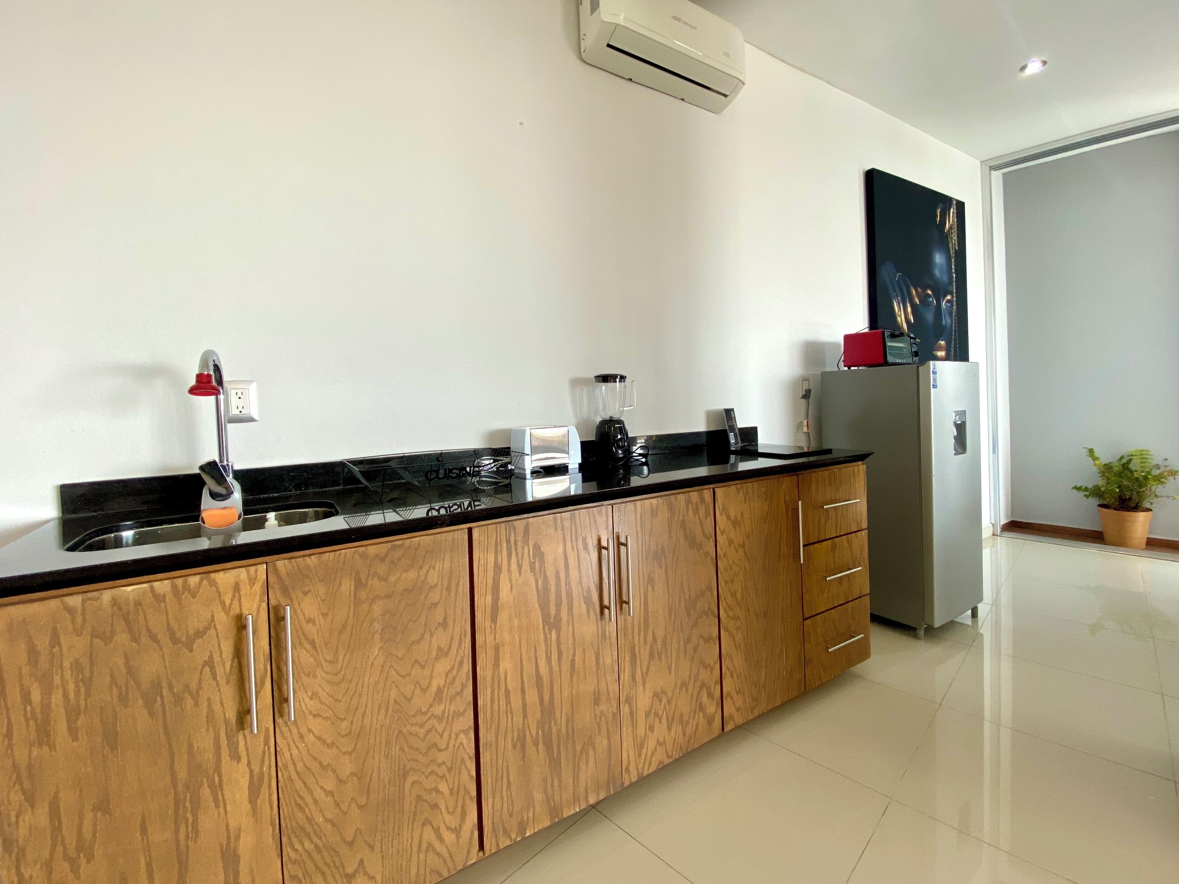 A modern kitchen with wooden cabinets, a black countertop, a built-in sink, a blender, a toaster, and a refrigerator.