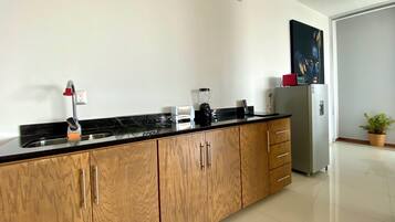 A modern kitchen with wooden cabinets, a black countertop, a built-in sink, a blender, a toaster, and a refrigerator.