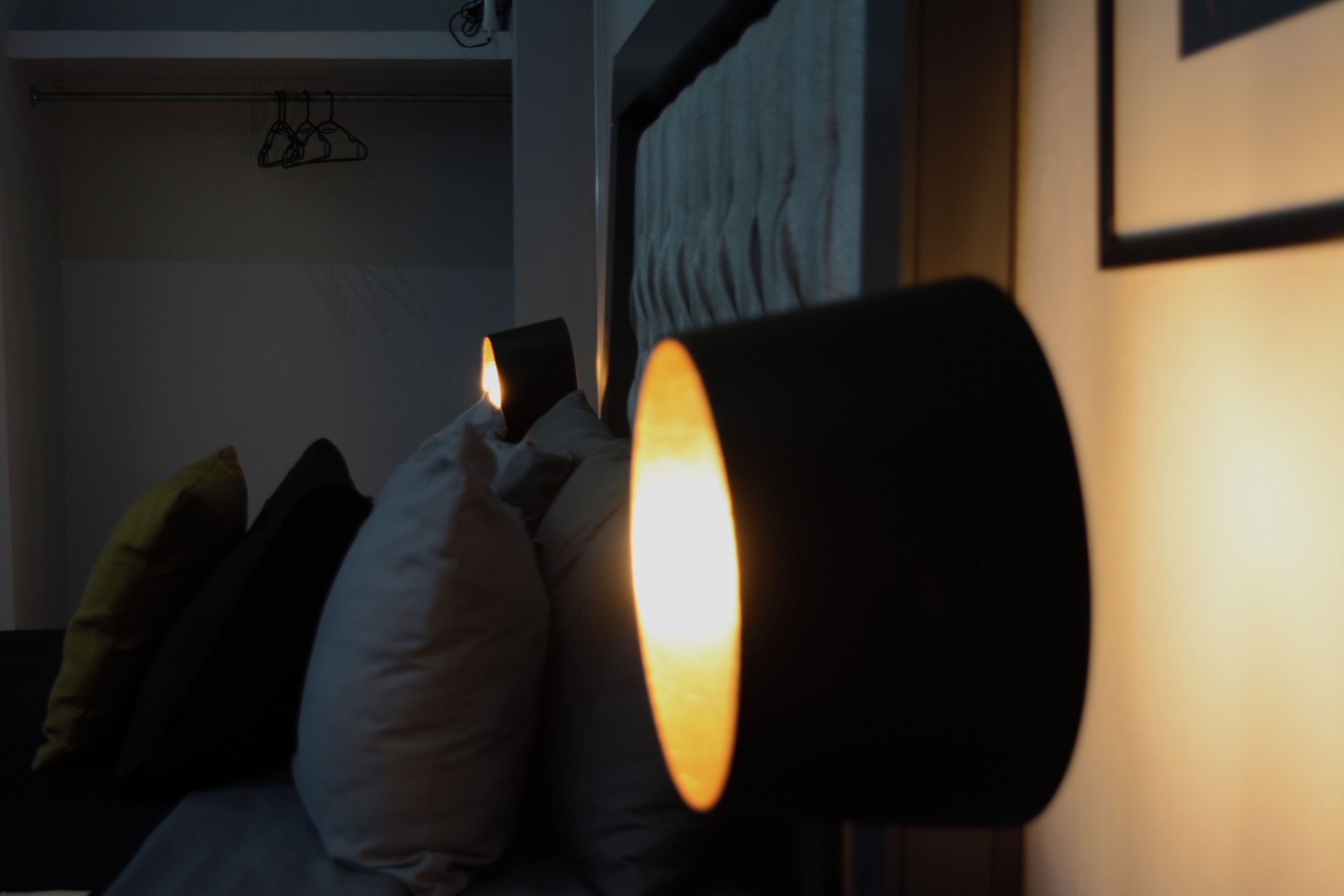 A dimly lit room with a bed, pillows, and a wall-mounted lamp.
