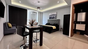 Een moderne hotelkamer met een zithoek, een bed met hoofdeinde, een badkamer met spiegel en wastafel, en uitzicht op de stad.