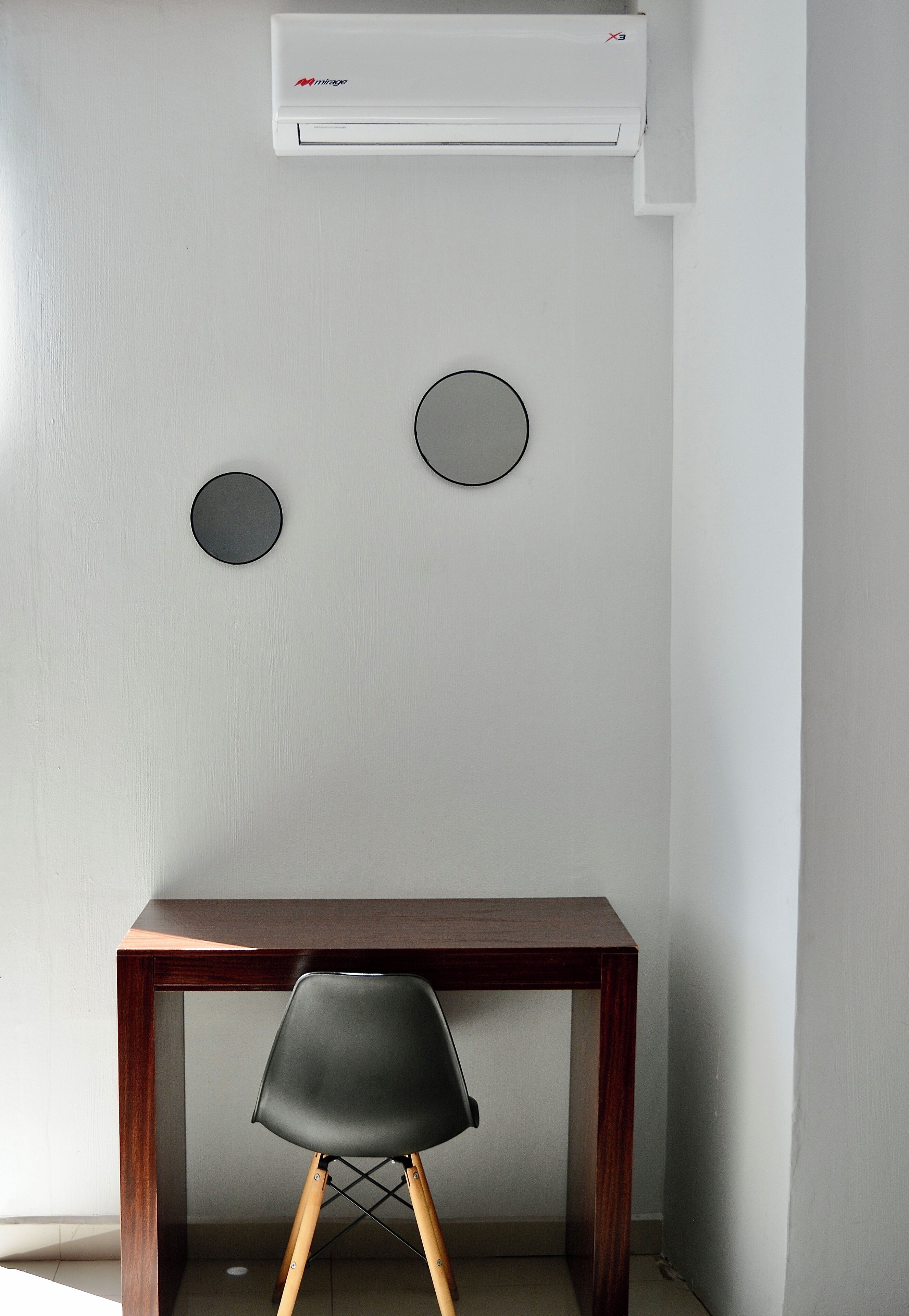 Una habitación con un escritorio de madera, una silla negra y un equipo de aire acondicionado en la pared.