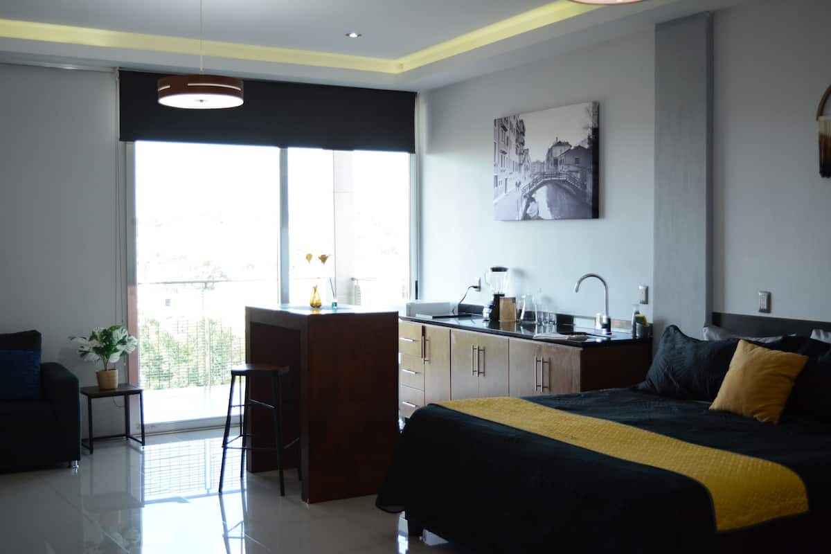 Een moderne hotelkamer met een groot bed, een klein kitchenette, een eethoek en een balkon met uitzicht.