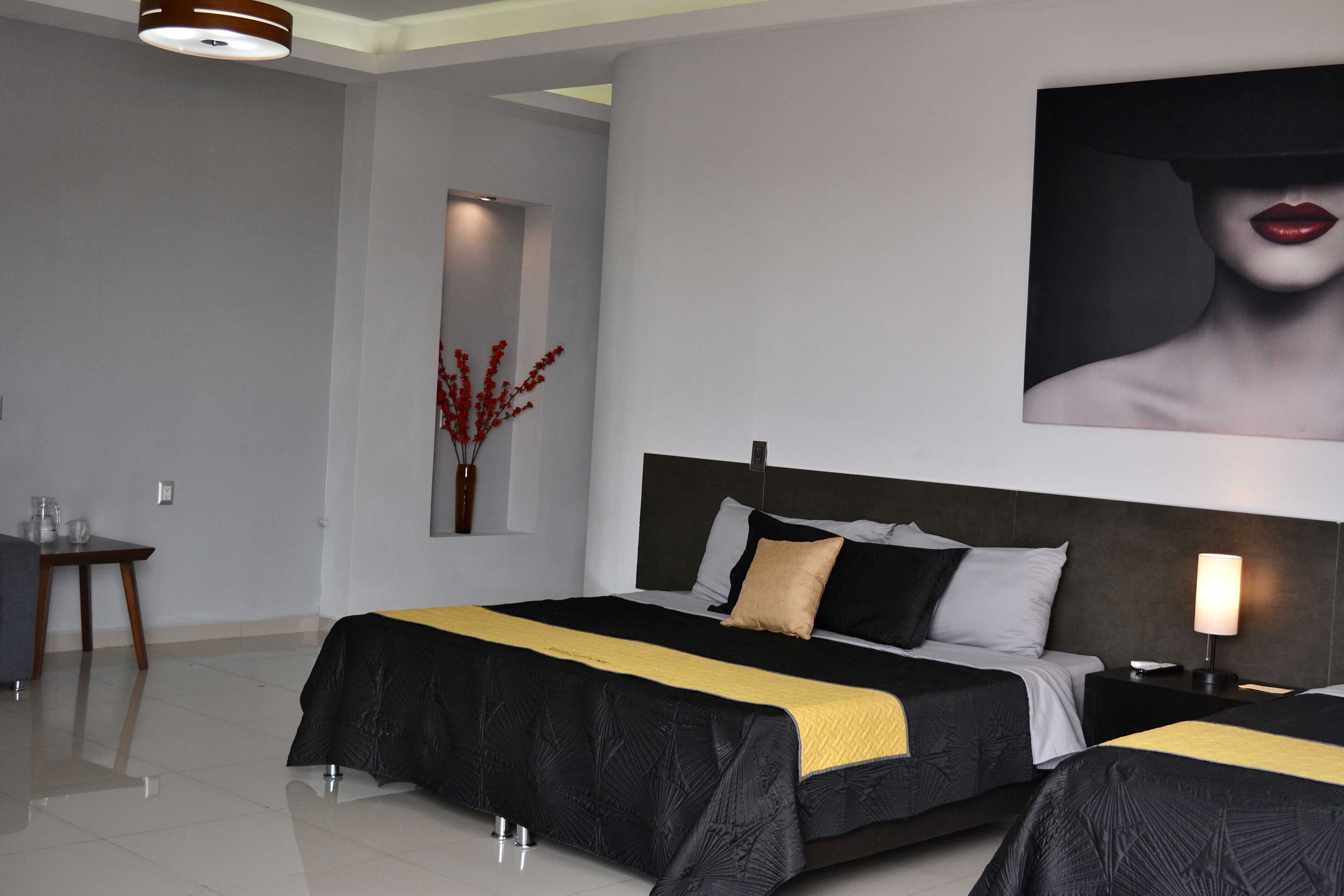 A modern hotel room with a large bed, bedside tables, a mirror, and a wall-mounted artwork.