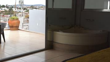 A room with a large window, a bathtub, and a potted plant on a balcony.