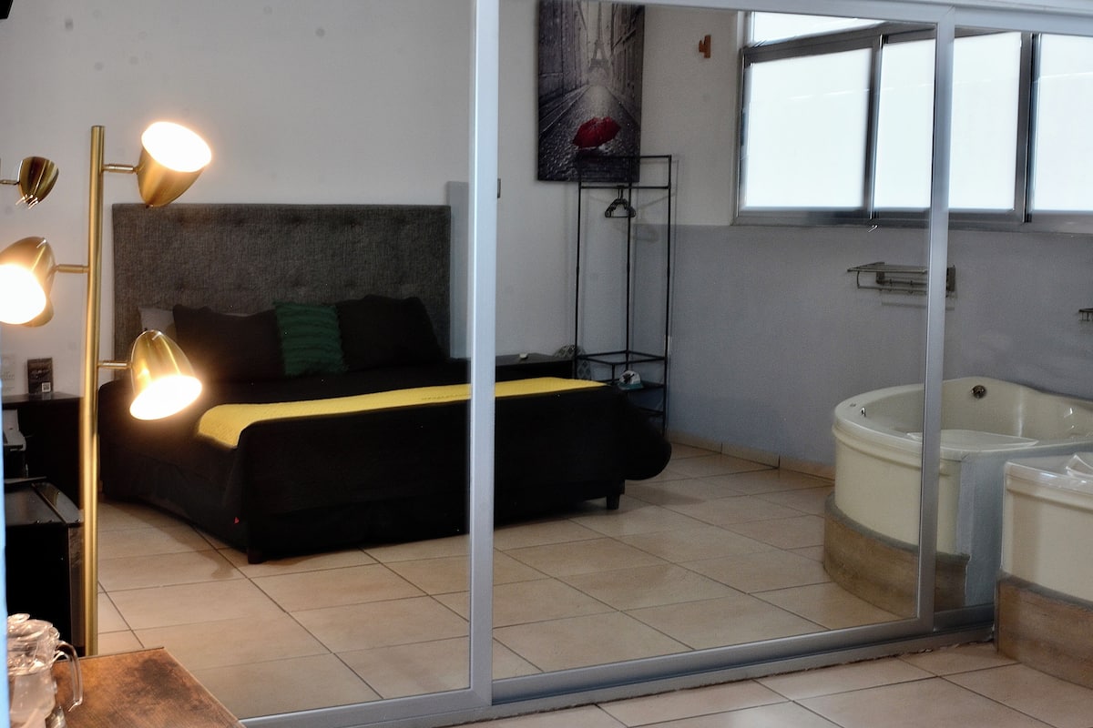 Een slaapkamer met een bed, nachtlampjes, een schilderij, een raam en een bad.