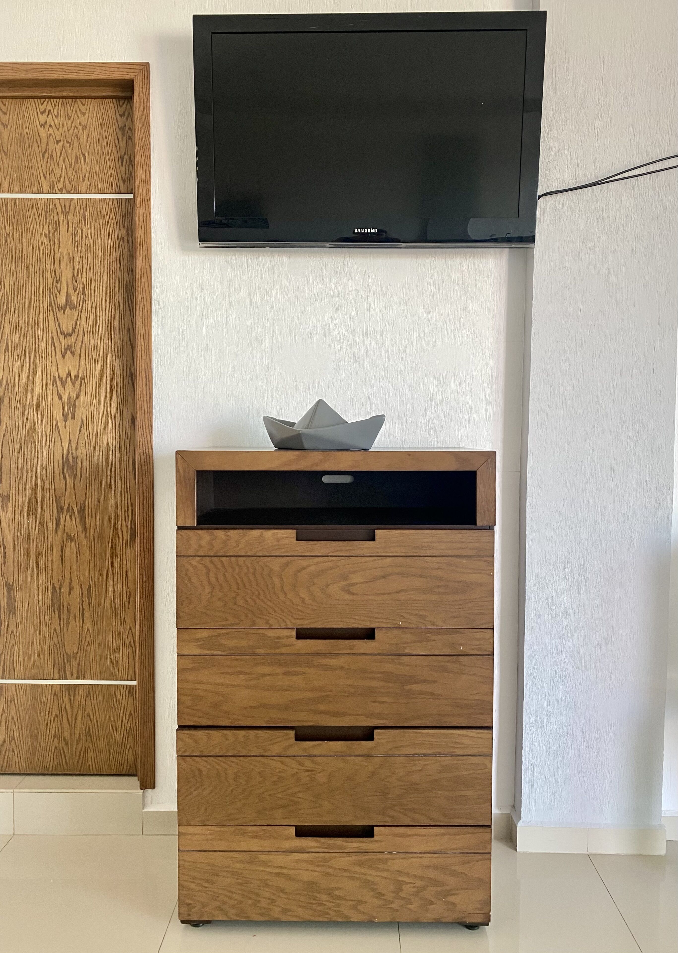 A wooden dresser with drawers and a flat-screen TV mounted on the wall above it.