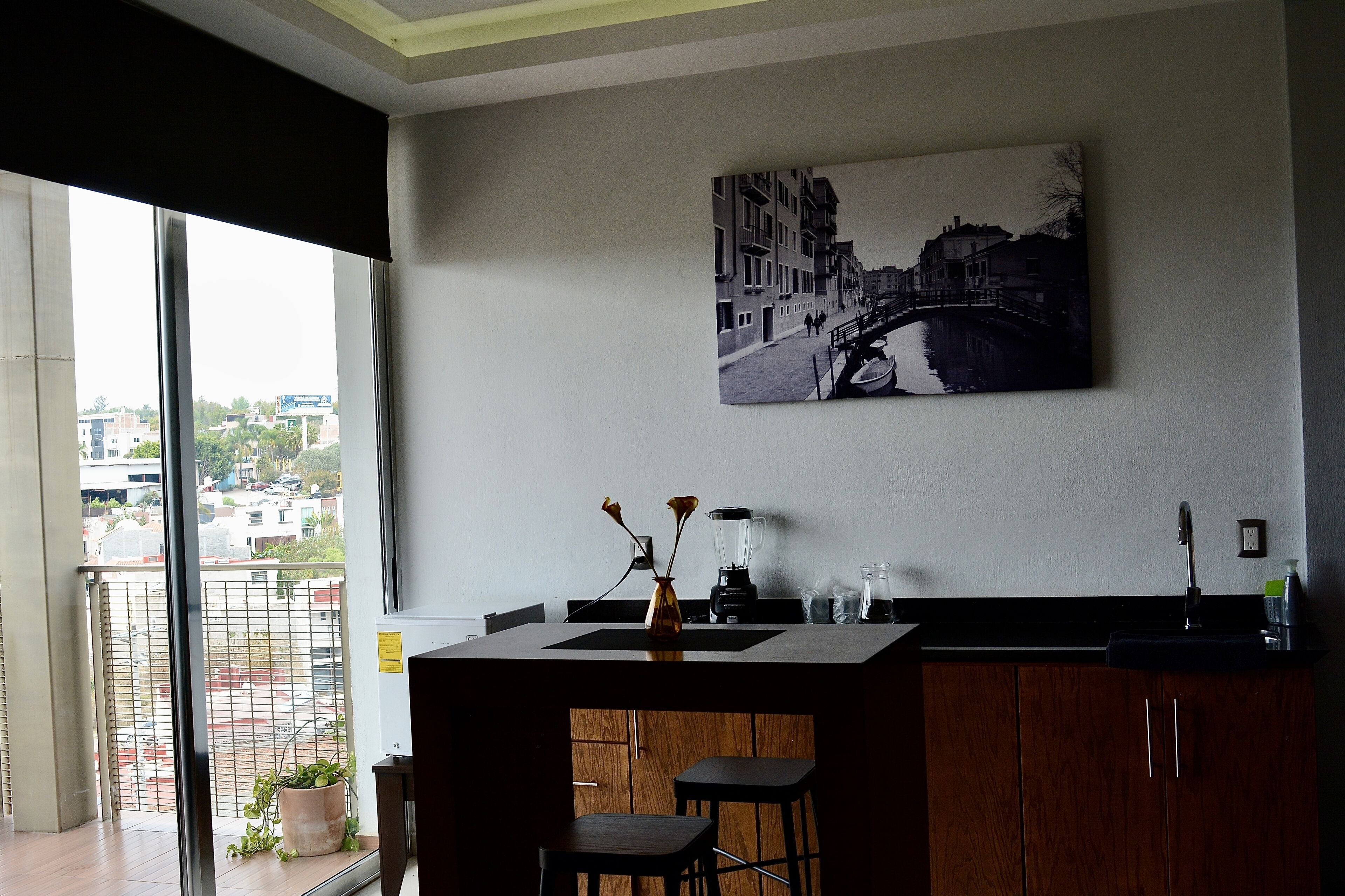 Una cocina moderna con un ventanal grande, un cuadro de un puente y una planta en maceta en el alféizar.