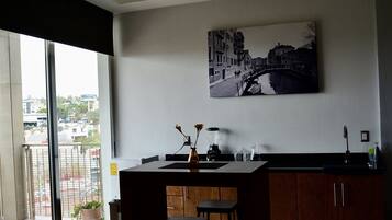 Una cocina moderna con un ventanal grande, un cuadro de un puente y una planta en maceta en el alféizar.